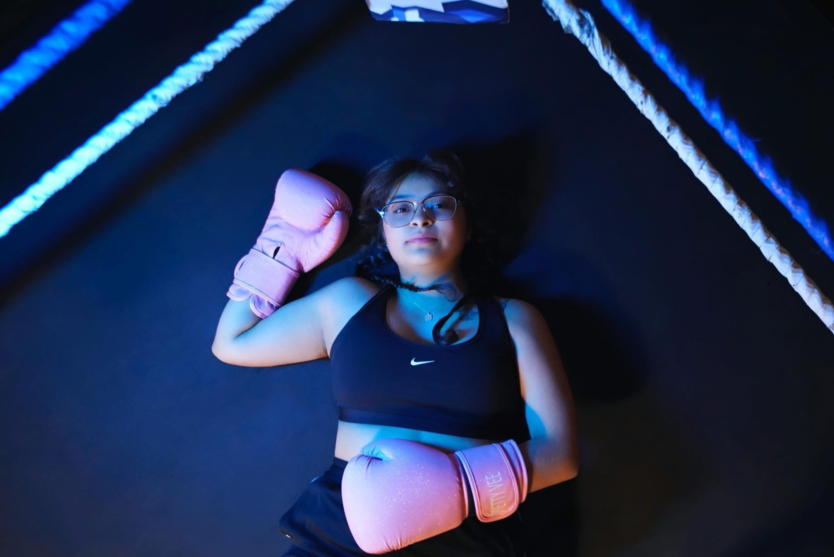 Overhead portrait of a boxer lying in the ring in pink gloves under blue and pink lights