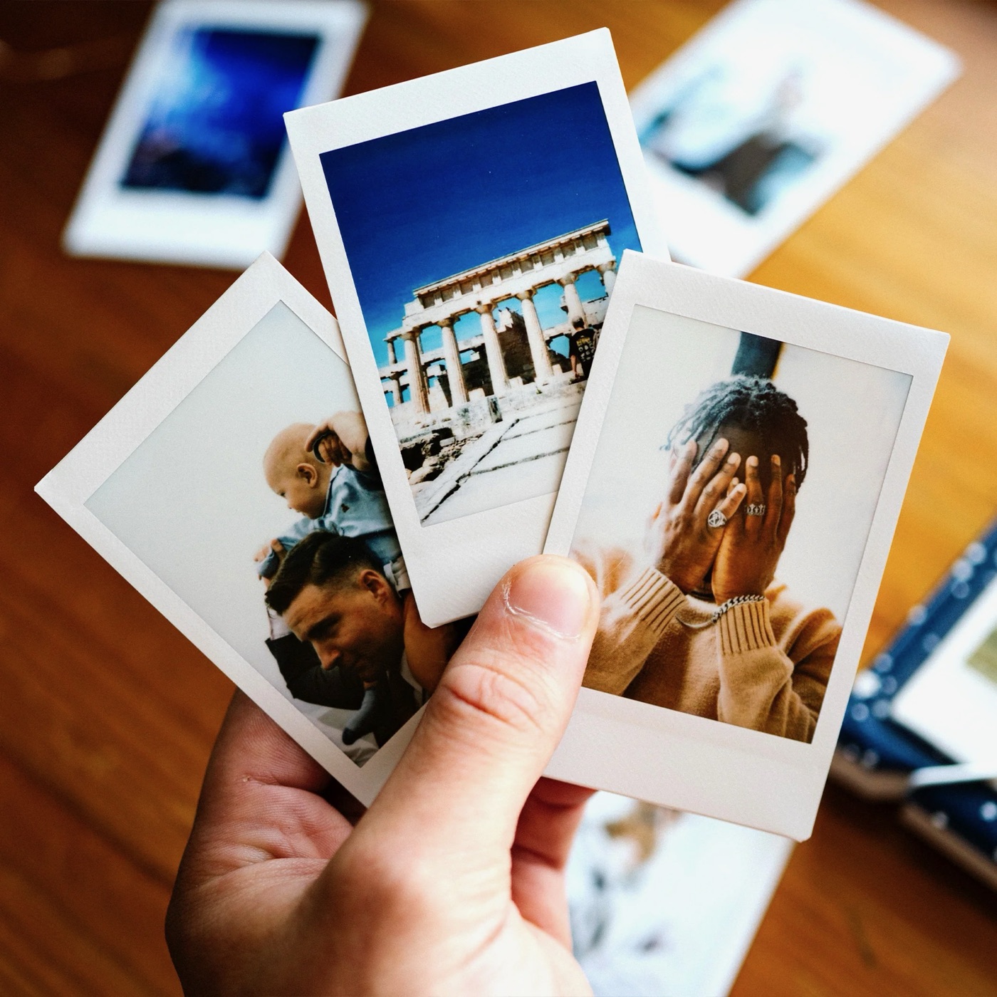 A hand holding three mini instant prints fanned out above a wooden table